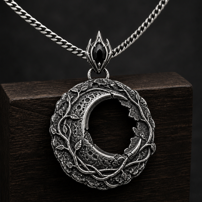 Oxidized 925 sterling silver hollow moon pendant with raised vine details, crater-like texture, ornate bail and included curb chain on a black background.