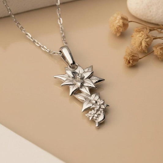 Close-up of the Lily Flower Necklace pendant on a neutral surface beside dried flowers
