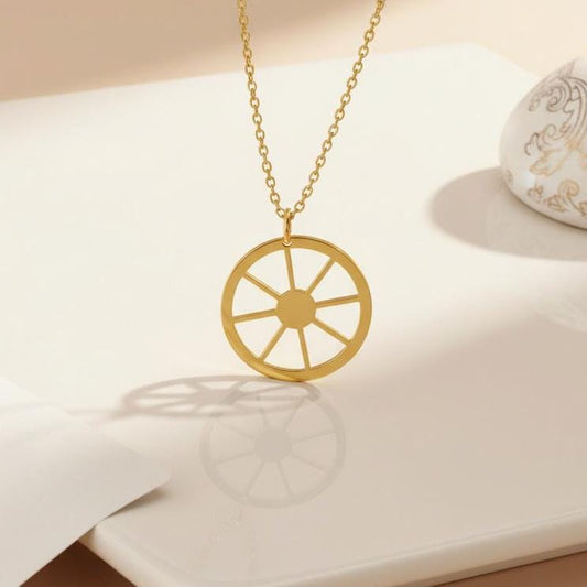 Gold Plated Silver Sun Symbol Necklace with an eight-spoke wheel pendant displayed on a white book