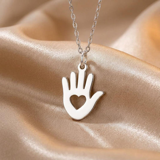 Close-up of the Helping Hand Necklace pendant with an open heart cutout on champagne satin