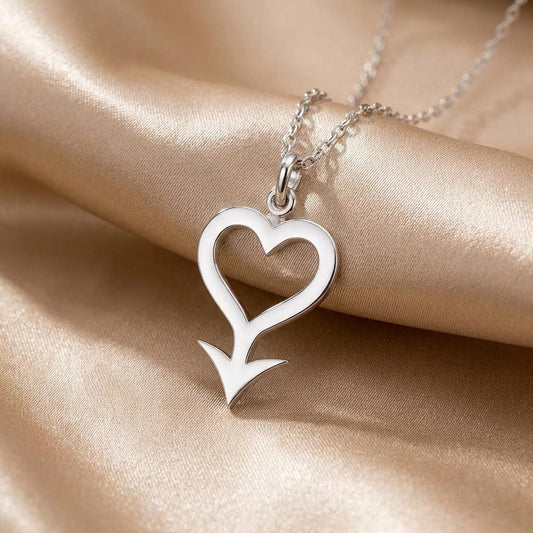 Close-up of the Cupido Symbol Necklace pendant with open heart and arrow detail on satin fabric