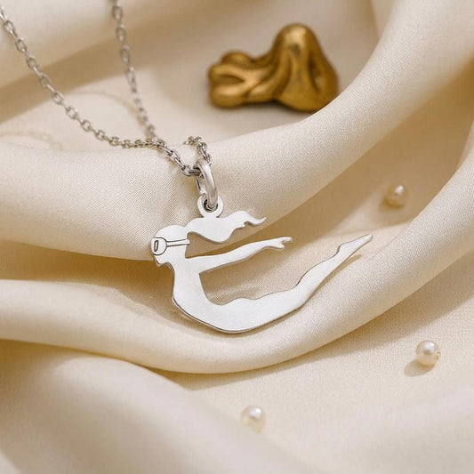 Close-up of the Diver Woman pendant on cream satin, showing the mask detail, curved body, and raised fin