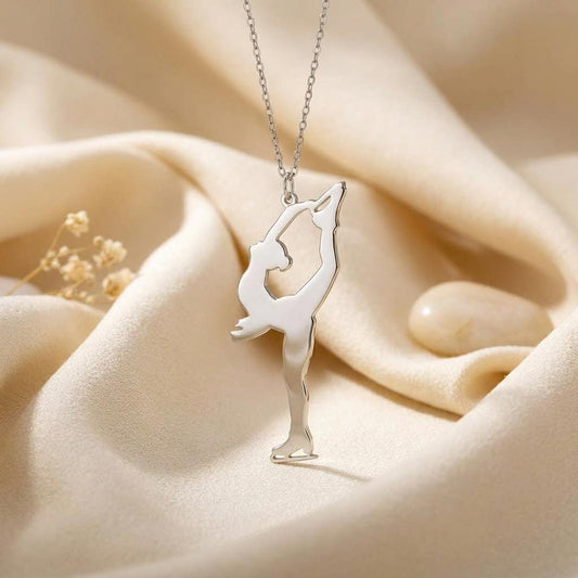 Close-up of the Figure Skater Necklace on cream satin, showing both hands holding a raised skate above the skater’s head
