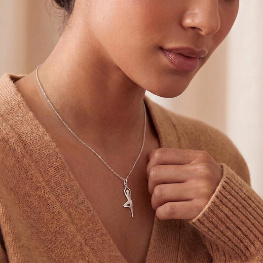Side view of a raised-leg yoga figure necklace worn with a brown cardigan