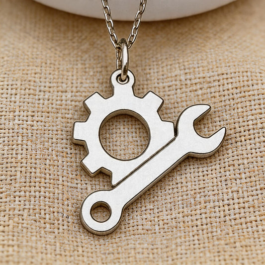 close-up of the Engineer Gear and Wrench Necklace pendant on textured beige fabric