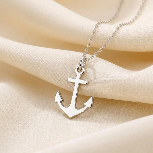 Close view of a polished anchor pendant on a fine chain over cream fabric