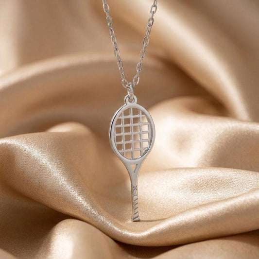 Silver Tennis Racket Necklace close-up with oval string-grid head and diagonally lined handle on champagne satin